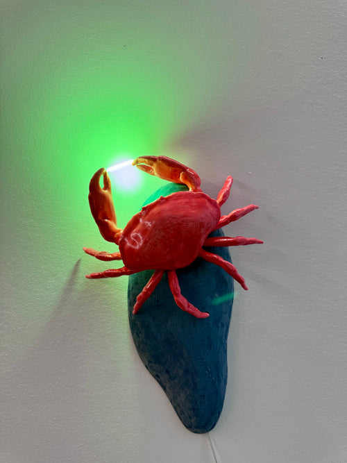 Red crab figurine on a blue rock with a green light in the background